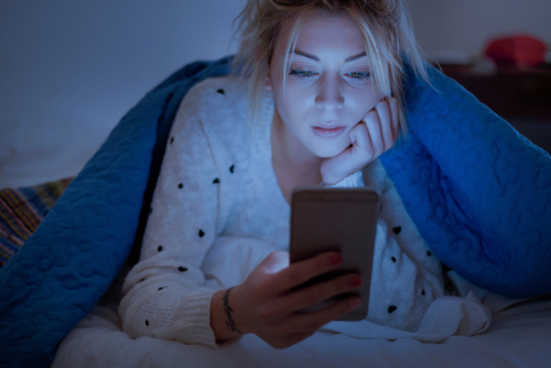 Woman in bed looking at her phone screen in a dark room