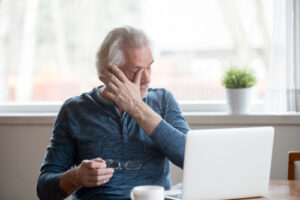 man wiping his eyes while on laptop