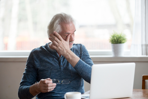 Fatigued older man rubbing his eyes in front of a computer