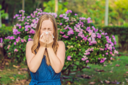Woman outside experiencing seasonal allergies sneezing into a tissue