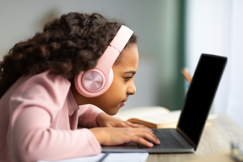 Little girl wearing headphones looking close at a laptop screen
