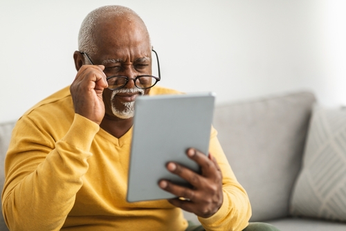 Older man looking over his glasses to read a tablet screen